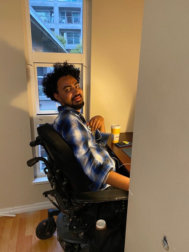 Ali Alsharahnee at his desk beside a window, headphones in, phone in hand, mid-call.